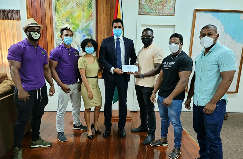 Minister of Culture, Youth and Sport Charles Ramson Jr (centre) presents a sponsorship cheque to president of the Guyana Bodybuilding and Fitness Federation, Keavon Bess, in presence of some contestants and officials.