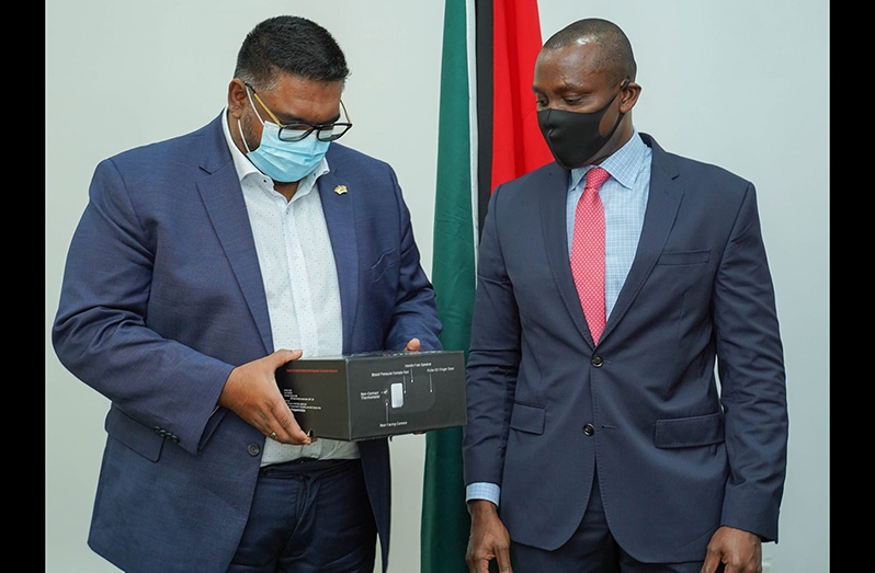 President, Dr. Irfaan Ali examines medical device presented to him by Dr. Deon Vigilance