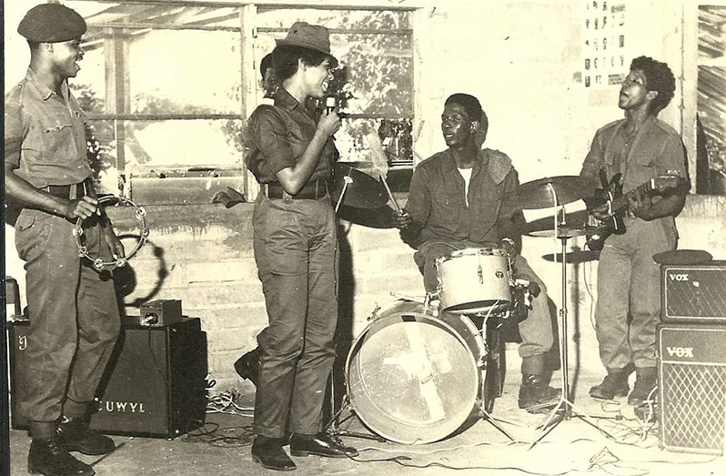 Capt. Cheryl Moore, standing with microphone,  singing Christmas carols at the GDF Camp at Lethem, Rupununi, 1973