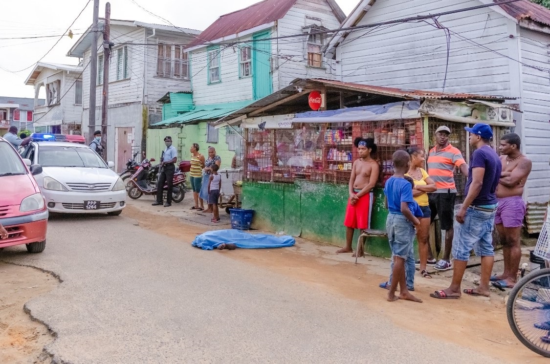 Police and residents of Albouystown surround the covered body of Cush after he was shot while purchasing cigarette (Delano Williams photo)