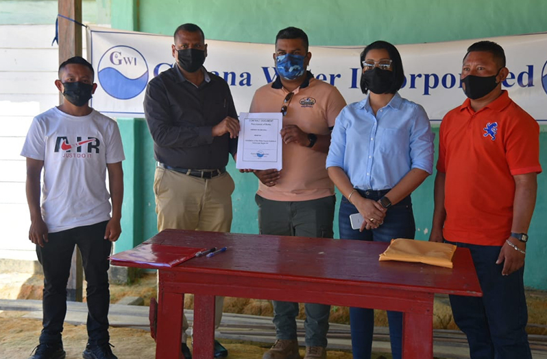 Minister of Housing and Water, Collin Croal (second left) hands over the signed contract to the Managing Director of R. Kissoon contracting services, Rudranauth Roopdeo, in the presence of others