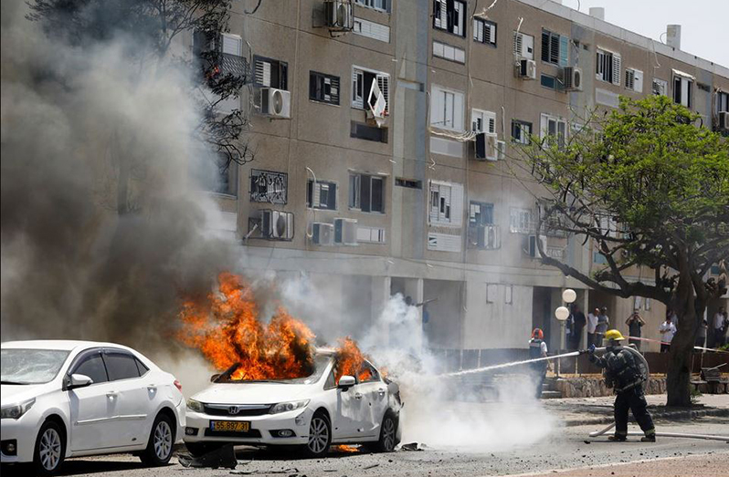 Israeli firefighters extinguish a car which caught on fire after a rocket was launched from the Gaza Strip, in Ashkelon, southern Israel May 11, 2021 (REUTERS/Nir Elias)