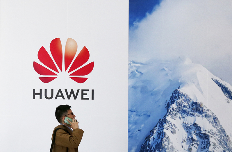 A visitor uses his mobile phone while passing by the stand of Huawei during an industry expo in Beijing. [Photo provided to China Daily]