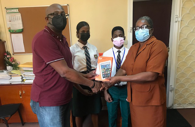 President of the New York Chapter, Wayne Knight, hands over the tablets to Headmistress of Bishops’ High School, Marilyn Gibson, in the presence of students, Shinia Daniels and Shakeel Babb