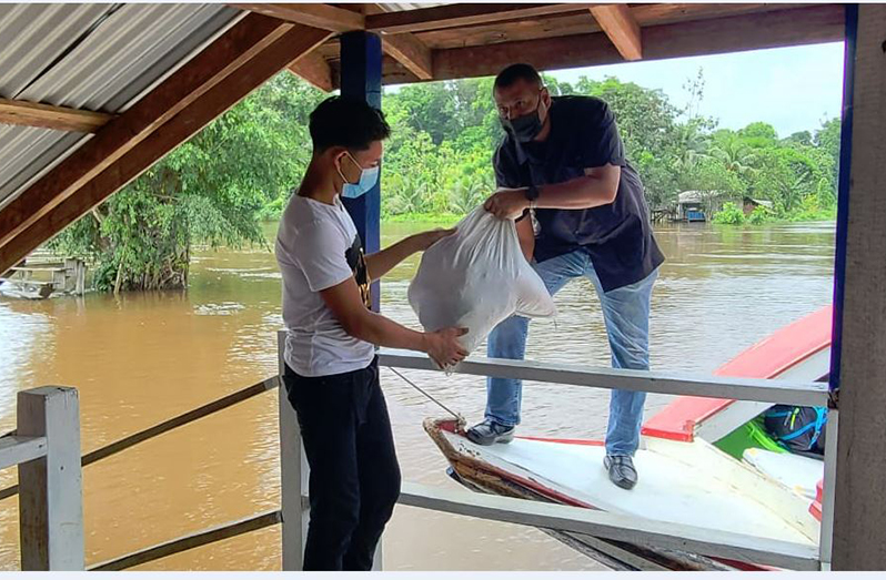 Minister of Housing and Water, Collin Croal, helping to offload a hamper from a boat to a flood-affected resident