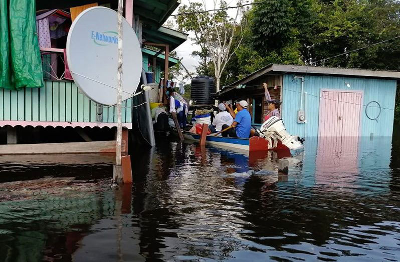 Persons in a boat manoeuvre through floodwater in Kwakwani to reach residents who are affected. Due to the flooding situation this is the only way for residents to move around (Solomon McGarrell photo)