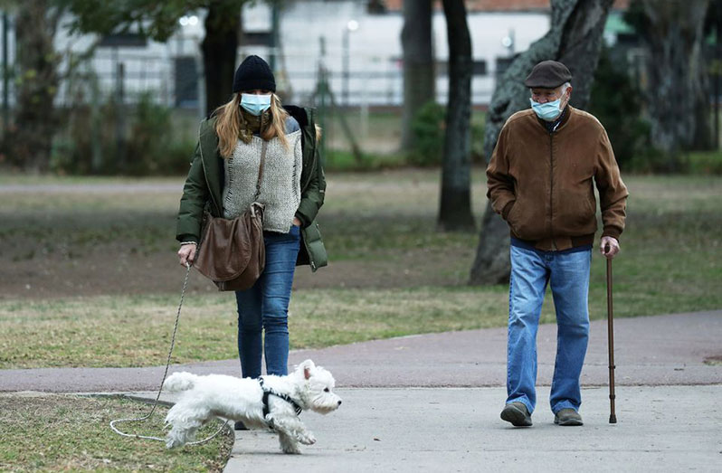 People wearing face masks walk their dog at a park during a national holiday as the number of the coronavirus disease (COVID-19) infections decreases, in Buenos Aires, Argentina