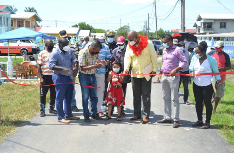 Four-year-old Anaya Ramotar assists Minister of Public Works, Juan Edghill, in cutting the ribbon to commission Bacchus Street, Zorg-en-Hoop, Region Five