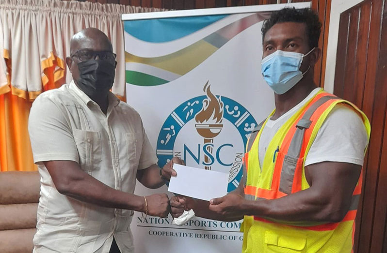 Director of Sport, Steve Ninvalle (L), hands over a cheque for an undisclosed sum to Carlos Peterson-Griffith towards his participation at the 2021 World Classic Powerlifting Championships in Halmstad, Sweden.