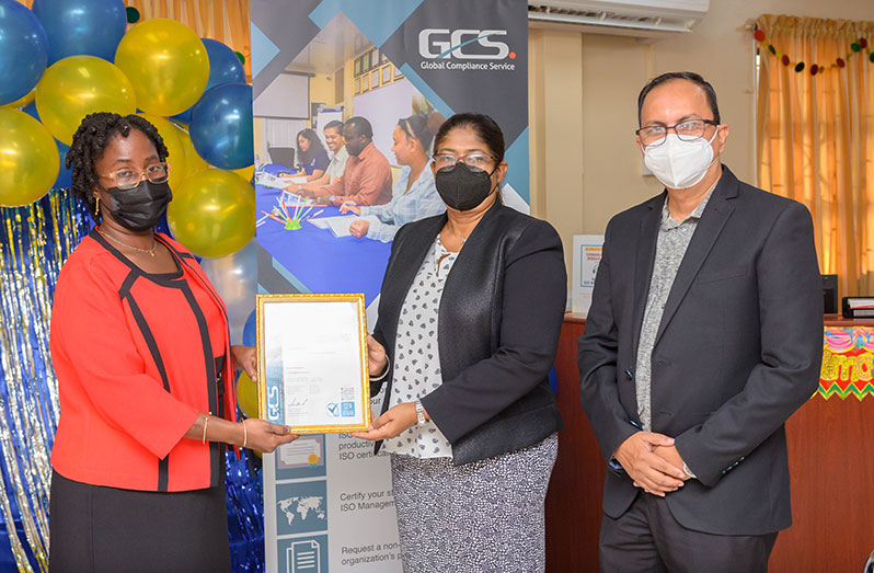 Global Compliance Service Guyana Inc.’s  Chief Executive Officer Candelle Bostwick, hands over the ISO certificate to Dr. Michelle Shiwnandan and her husband Dr. Ravindra Shiwnandan