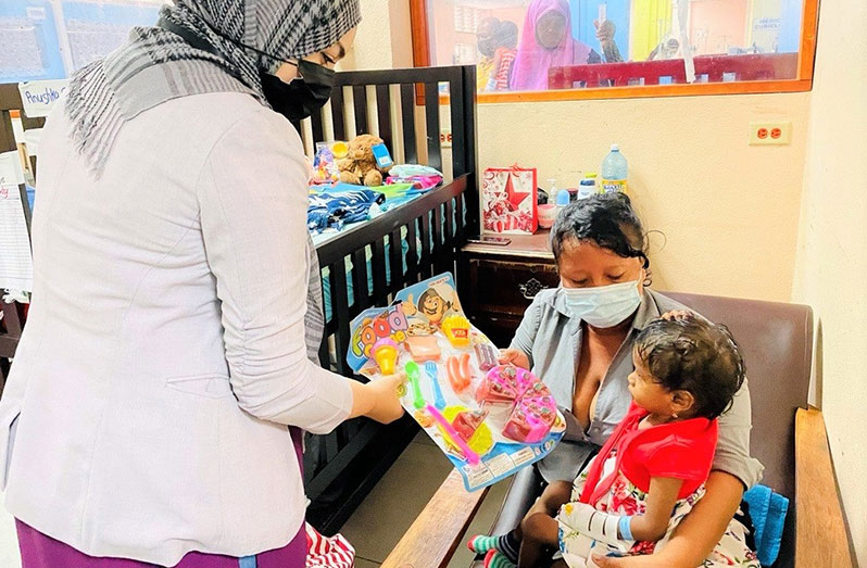 Marketing Officer at GNBS, Aishah Hussain, presenting a toy to a child in the Paediatric Ward