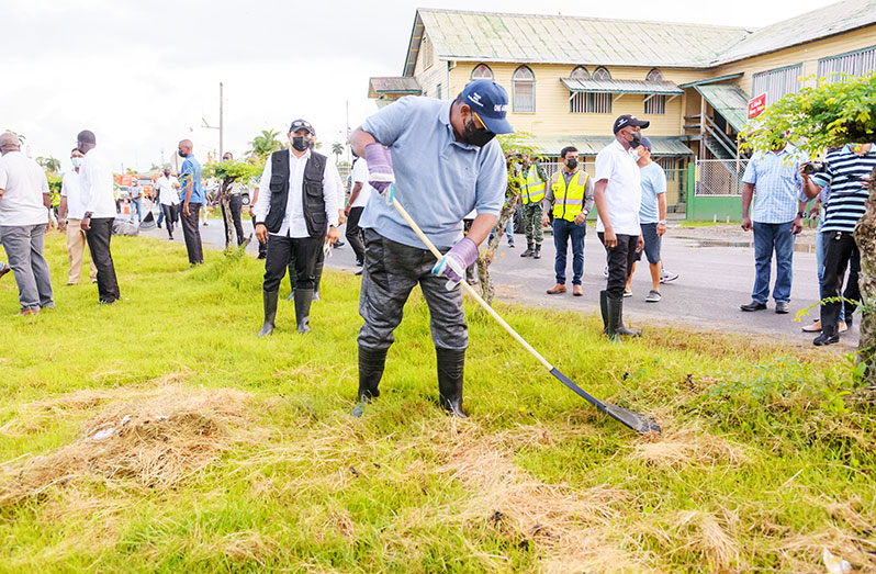 President Dr. Irfaan Ali (left) removing dried grass and weeds from the median at Vlissengen Road and Hadfield Street during the clean-up exercise on Saturday (Delano Williams photo)