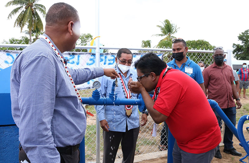 Finance Minister, Dr. Ashni Singh, drinks water from the new system as Minister of Housing and Water, Collin Croal and others look on (Ministry of Housing photo)