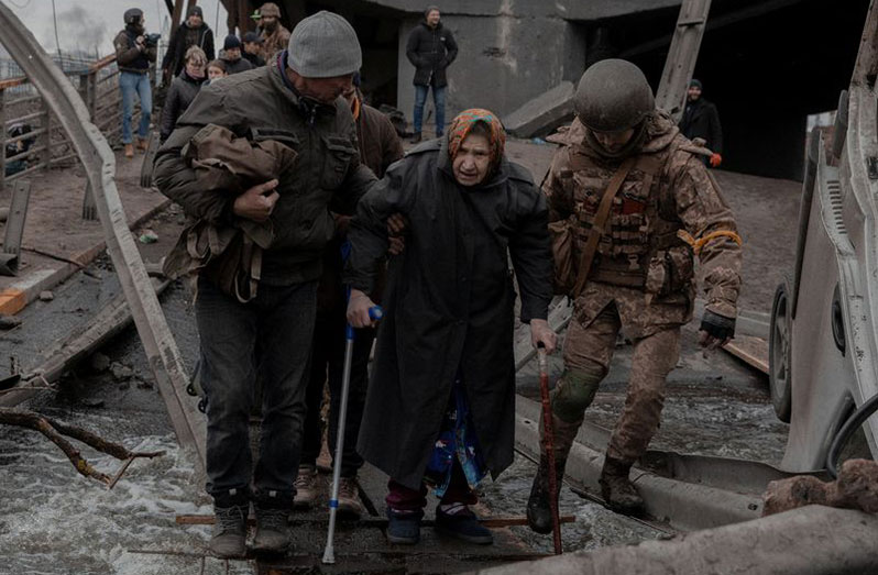An elderly woman is helped while crossing a destroyed bridge as she tries to leave the city of Irpin, in the Kyiv region, Ukraine