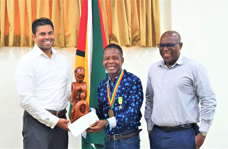 Sport Minister Charles Ramson Jr (left) makes the presentation to Olympic medallist, Michael Parris, in the presence of Director of Sport, Steve Ninvalle (Photo: News Room/April 27, 2022)