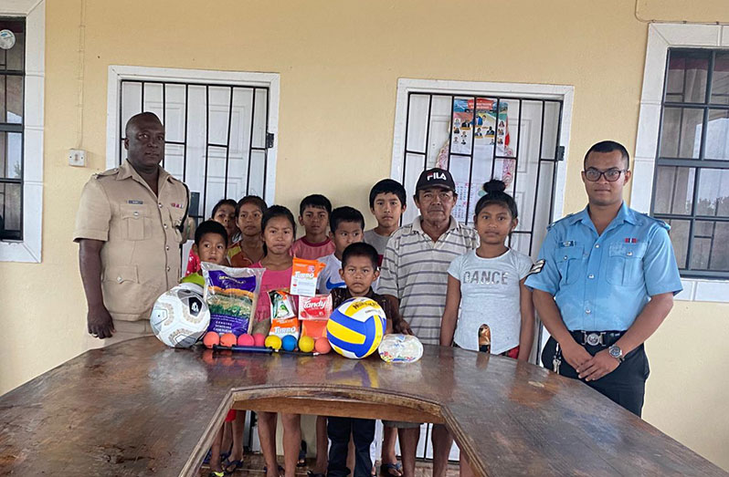 ASP Oswald Pitt (left), Sergeant Hakim (right) and Deputy Toshao Isaac Williams with some of the members of the police youth club and several of the donated items
