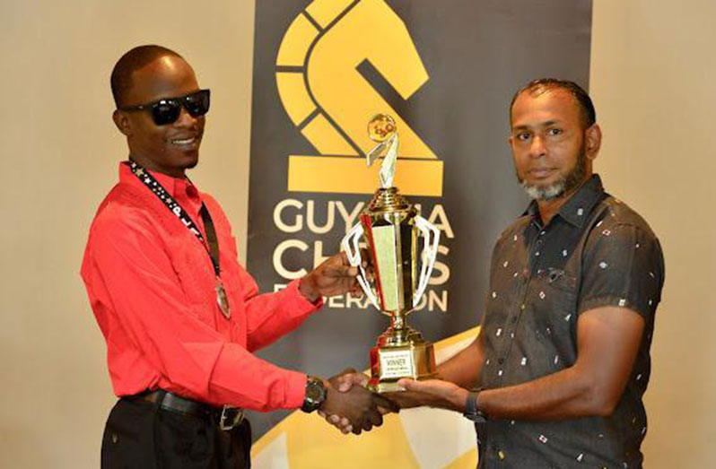 Winner of the 2022 National Chess Championship, CM Wendell Meusa (left), receives his trophy from executive member of the GCF, Irshad Mohamad