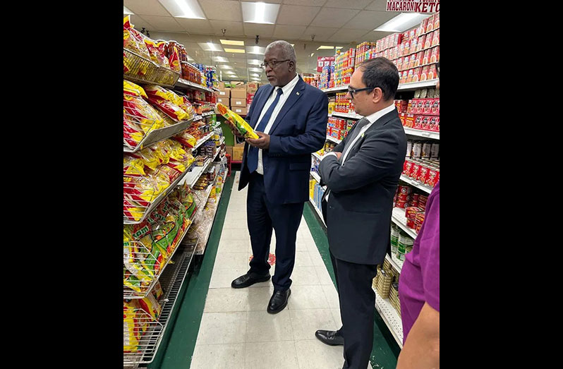 Prime Minister, Brigadier (Ret’d) Mark Phillips, inspecting one of the many Guyanese items on the shelves, as Deputy Chief of Mission, Zulfikar Ali, looks on (OPM photo)