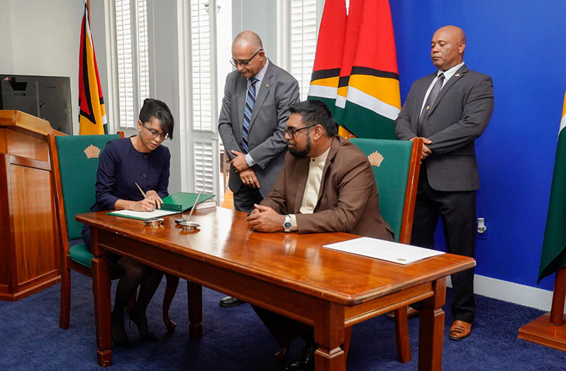 Newly-sworn in Commissioner Ms. Pauline Chase signs the official appointment document alongside President Dr. Irfaan Ali