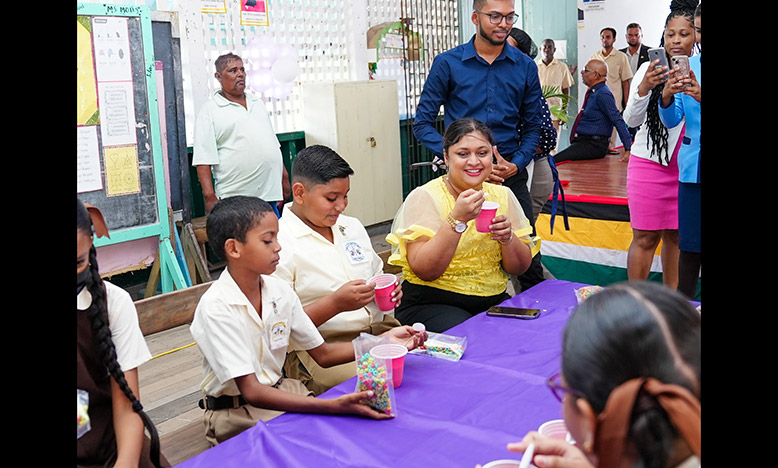 Education Minister Priya Manickchand sits with two pupils of the Windsor Forest Primary School as the breakfast programme’s coordinator, Mahendra Phagwah looks on (Education Ministry photo)