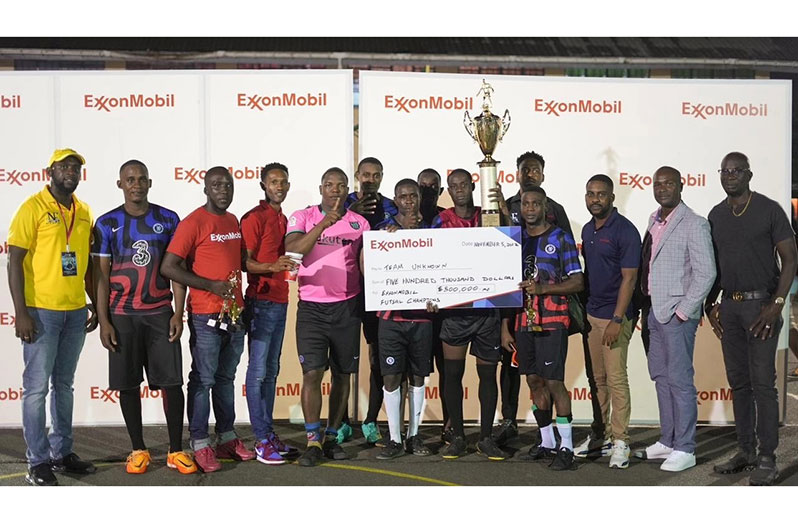 The victorious Team Unknown unit displaying the championship trophy in the presence of tournament officials and representatives from sponsors at the end of the ExxonMobil Futsal Championship.