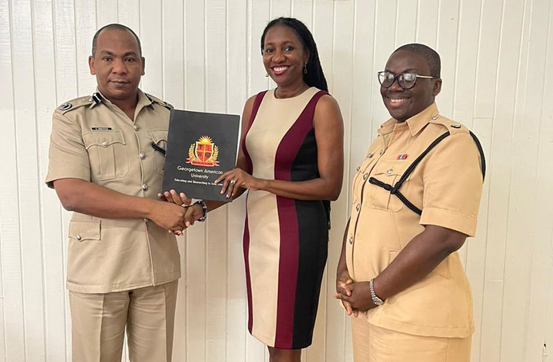 Deputy Commissioner of Police (Administration), Dr. Calvin Brutus and Dr. Melissa Varswyk, Chief Executive Officer of Georgetown American University, display the folder containing the signed Memorandum of Agreement, in the presence of Superintendent Nicola Kendall, Strategic Planning Officer