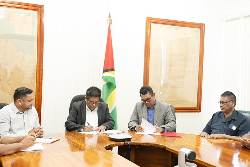 Senior Minister within the Office of the President with responsibility for Finance, Dr Ashni Singh and General Manager of  Demerara Bank Limited, Dowlat Parbhu, sign the agreement as Minister of Natural Resources, Vickram Bharrat and other officials look on (Delano Williams photo)