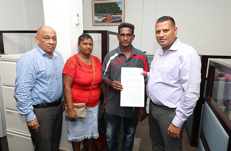 Minister of Housing and Water, Collin Croal (right) hands over an Agreement of Sale to one of the families at the CH&PA Office, as CH&PA Director of Community Development, Gladwyn Charles (left) looks on