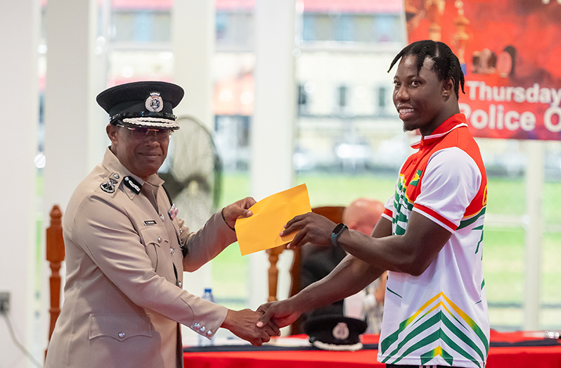 Acting Commissioner of Police, Clifton Hicken presents Emanuel Archibald, Guyana’s first gold medalist in the 100m event at the Central American and Caribbean (CAC) Games, with a monetary award (Delano Williams photo)