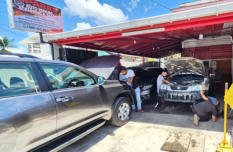 Martin Ramdeen services a Toyota Landcruiser at his D'Urban Street, Lodge Georgetown mechanic shop as three other mechanic change parts on a Honda CRV