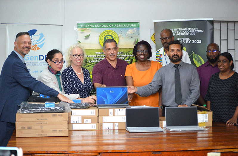 The handing over of laptops to the CEO of GSA, Mr. Gavin Ramnarine (second right), from the British High Commissioner to Guyana, Ms. Jane Miller (third from left), the IICA representative in Guyana/CARICOM Liaison, Mr. Wilmot Garnett (center), the Resident Coordinator, United Nations Guyana, Ms. Yesim Oruc (second left), the Permanent Secretary (PS) of the Ministry of Agriculture, Delma Nedd (fifth right), and other officials from IICA and GSA (Yohan Japheth photo)