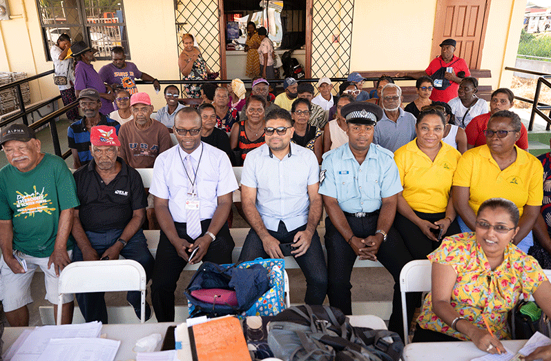 Proprietor of Mohamed’s Enterprise, Azruddin Mohamed, with some of the pensioners, staff, and police officers sitting on the donated benches at the Providence Police Station