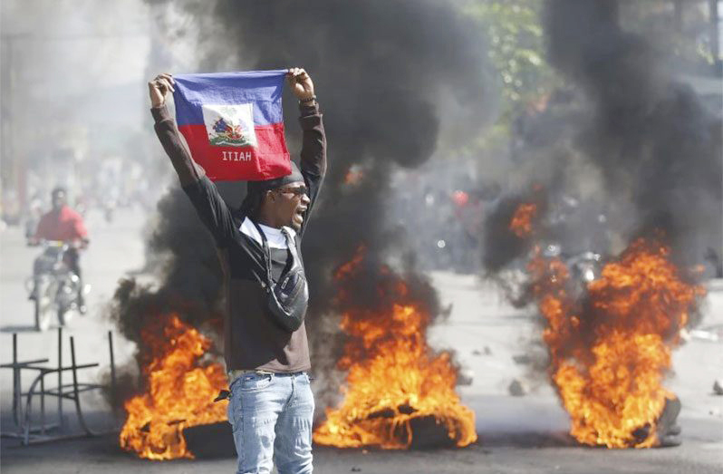 A demonstrator holds up a Haitian flag during fiery protests (Source: AP/Odelyn Joseph)