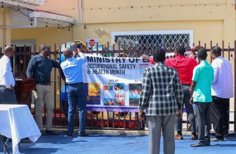 Occupational Safety and Health banner being mounted by Minister of Labour, Joseph Hamilton and persons from the ministry’s OSH Department