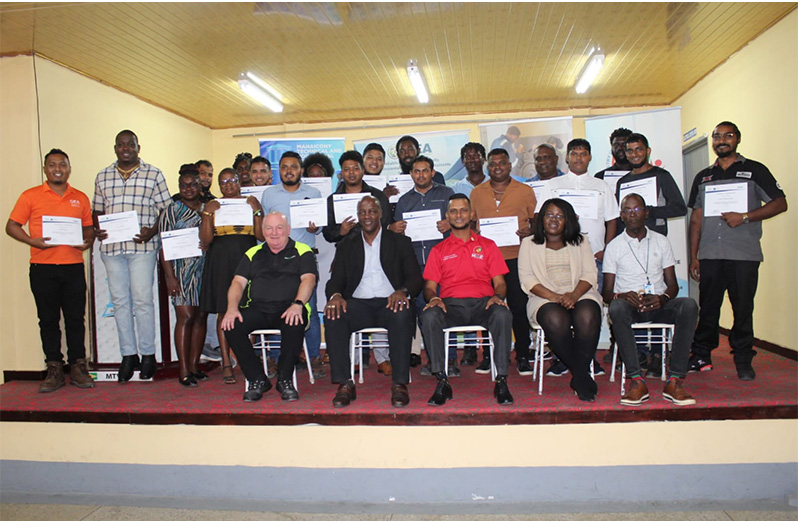 (From left to right) Mr. Steve Burr, Senior Trainer and Director, REVAMP Training Limited; Dr. Alfred King, Permanent Secretary, Office of the Prime Minister; Dr. Ritesh Tularam, Deputy Chief Education Officer (Technical) Ministry of Education; Ms. Shevon Wood, Deputy Chief Executive Officer, Guyana Energy Agency; Mr. Collis Best, Administrator, Mahaicony Technical and Vocational Education Training Centre along with participants who completed the fourth EV Maintenance and Repairs Training Programme