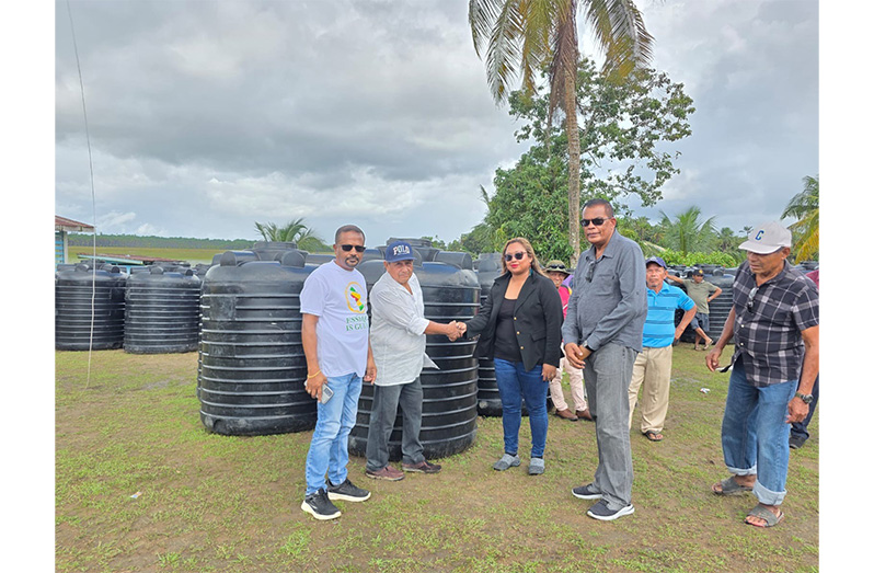 A resident receives a black tank from PPP/C Member of Parliament Dr Tandika Simone Smith as officials and other residents look on