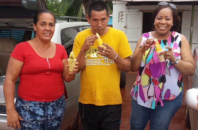 “This is what will always remind me of Kumaka,” says first-time customer and Welfare and Humanitarian Officer, Ms. Angela Grant, visiting from the USA.
     At left is Yonette Boyer cheerfully displaying a serving of boiled corn as the two others ‘dig into’ theirs.