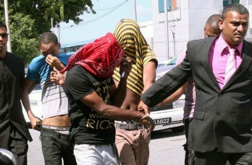 HIDING FACES: Cpl Majid Khan, right, escorts Kempton Harris, red bandanna over face, Nicholas Dean, second left, John Spann, in striped jersey, to the San Fernando Magistrates’ Court as they hid their faces yesterday. The three are charged with rape and also with robbing a family at their home.