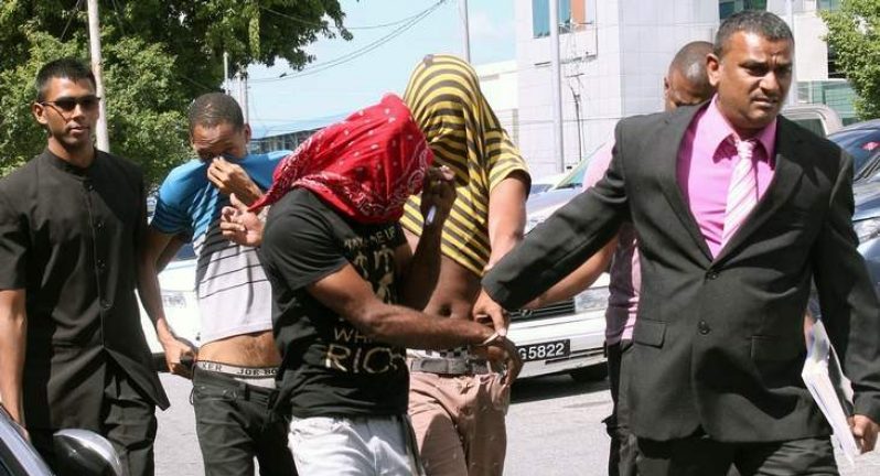 HIDING FACES: Cpl Majid Khan, right, escorts Kempton Harris, red bandanna over face, Nicholas Dean, second left, John Spann, in striped jersey, to the San Fernando Magistrates’ Court as they hid their faces yesterday. The three are charged with rape and also with robbing a family at their home.