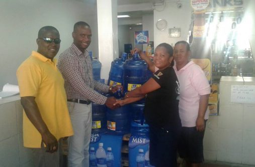 Banks Banks DIH Bartica Branch Manager, Brenda Murray, handing over the water to Mayor of Bartica, Gifford Marshall, in the presence of two residents