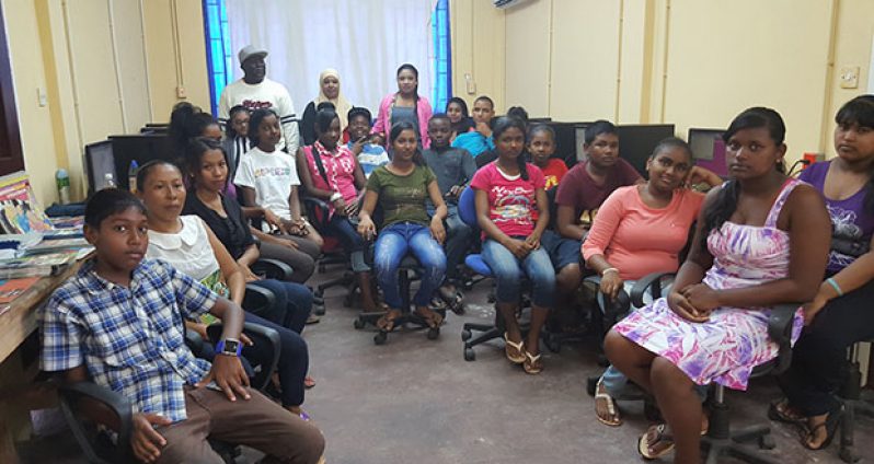 Commander ‘D’ Division, Stephen Mansell, Facilitator/Corporal Rockell Miguel, Chairperson of Belle West Youth Group, Nolle Readie (standing at the back) posing with youths that are part of the computer training programme