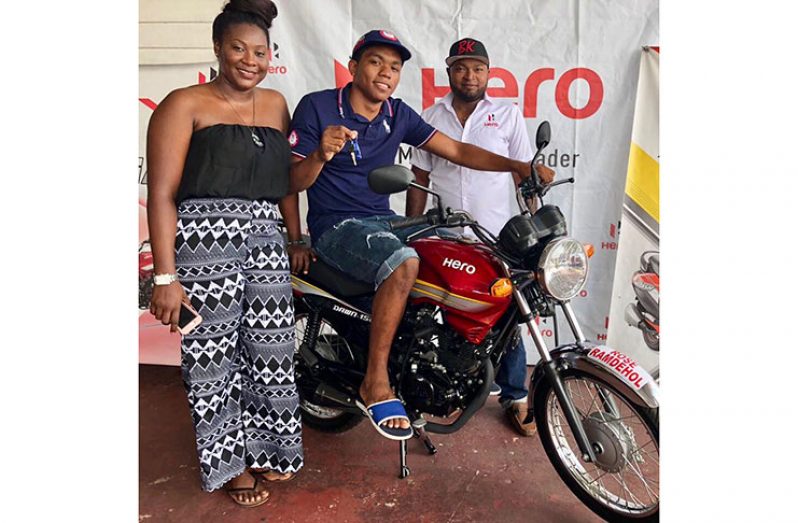 Phillip DeFlorimonte collects his prize of a motorcycle from Hero Motorcycle representative, Devon Pyle, and  Jacklyn Boodie of the Petra Organisation.
