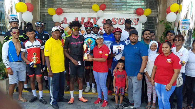 Briton John receives his cash prize and trophy from a representative of A. Ally and Sons while staff, race coordinators and other cyclists shared a photo moment.