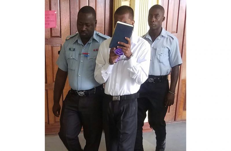 Jonathan Budhan hides his face with the Holy Bible, as police escorted him out of the courtroom