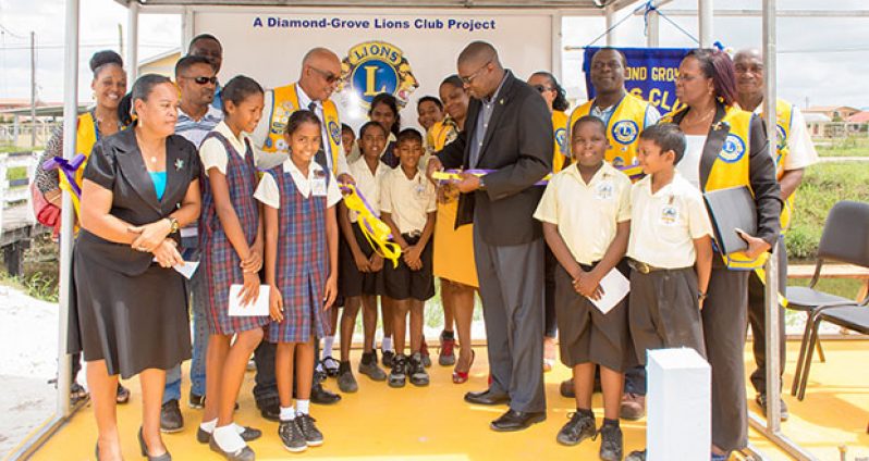 Public Infrastructure Minister David Patterson cuts the ceremonial ribbon in the presence of Lions Club members, students and teachers to officially commission one of several bus sheds within the Diamond Housing Scheme.