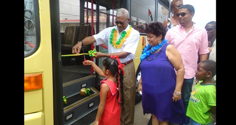 President David Granger assissts a Berbice girl to cut the ribbon commissioning the bus which will be used to transport students living between Adventutre to Gibraltar.
