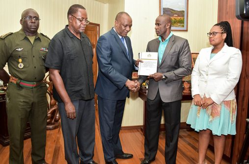 Minister of State, Joseph Harmon receives the report from Brigadier (Retired) Bruce Lovell as Lieutenant Colonel Denzel Carmichael, former Assistant Commission of Police, Mr. Winston Cosbert and Ms. Christine Bailey look on.