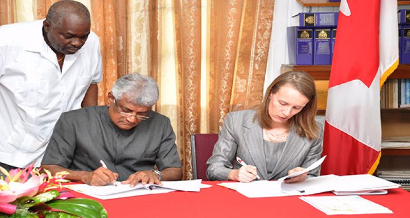 From left, GECOM Chairman, Dr Steve Surujbally, and Canadian High Commissioner, Nicole Giles, sign the $7.9M contribution agreement. Standing is CEO, Keith Lowenfield (Photo by Delano Williams)