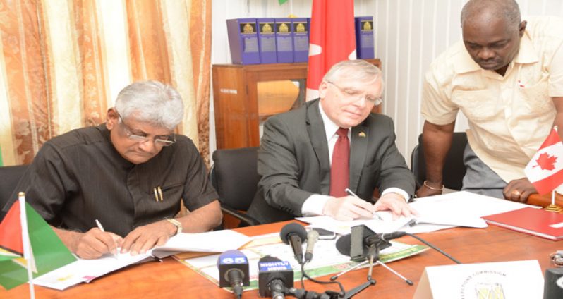 Canadian High Commissioner Pierre Giroux (right) and GECOM’s Chairman, Dr Steve Surujbally (left) sign an agreement on Monday at the Commission’s Kingston office in the presence of Chief Elections Officer Keith Lowenfield (extreme right)
