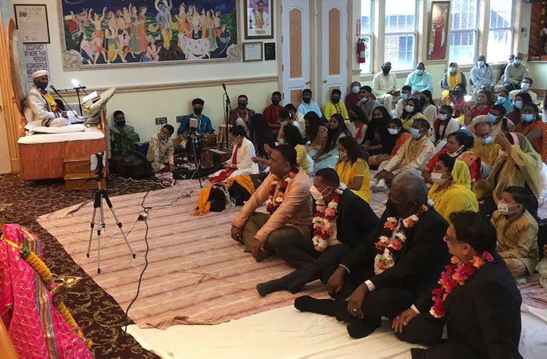Prime Minister Mark Phillips and Housing and Water Minister Collin Croal join the congregation in listening attentively to a pandit during a visit to a mandir in New York on Sunday